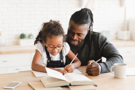 Father helping child with work at table.