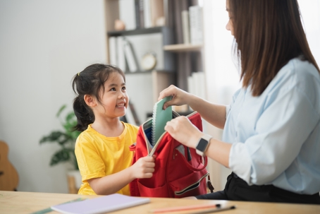 mother helping daughter pack school bag
