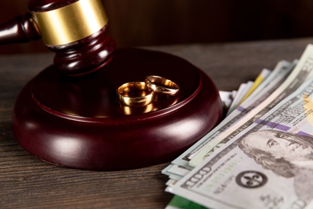 Gavel with wedding rings and stack of money.